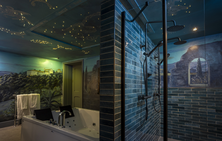 Bathroom with a tiled shower and a bathtub, featuring blue-green tiles and walls painted with landscape murals and a ceiling with star-like lights.