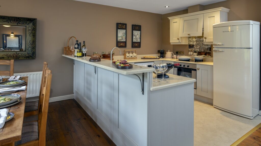 CASTLE LESLIE INTERIORS Modern kitchen with white cabinets, a countertop island, and a vintage-style white refrigerator; dining table is set for a meal, and wine glasses are on the counter.