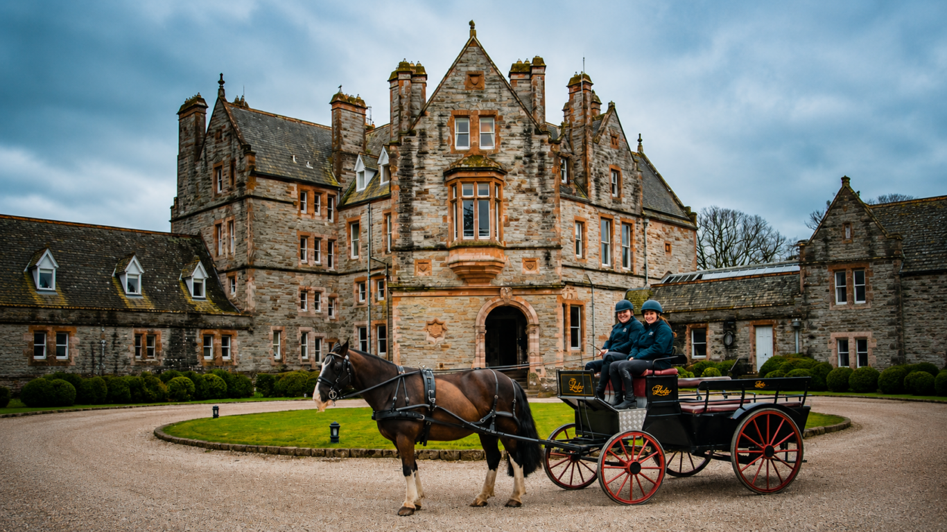 A horse-drawn carriage with two people sits in front of a large, historic stone mansion on a cloudy day.